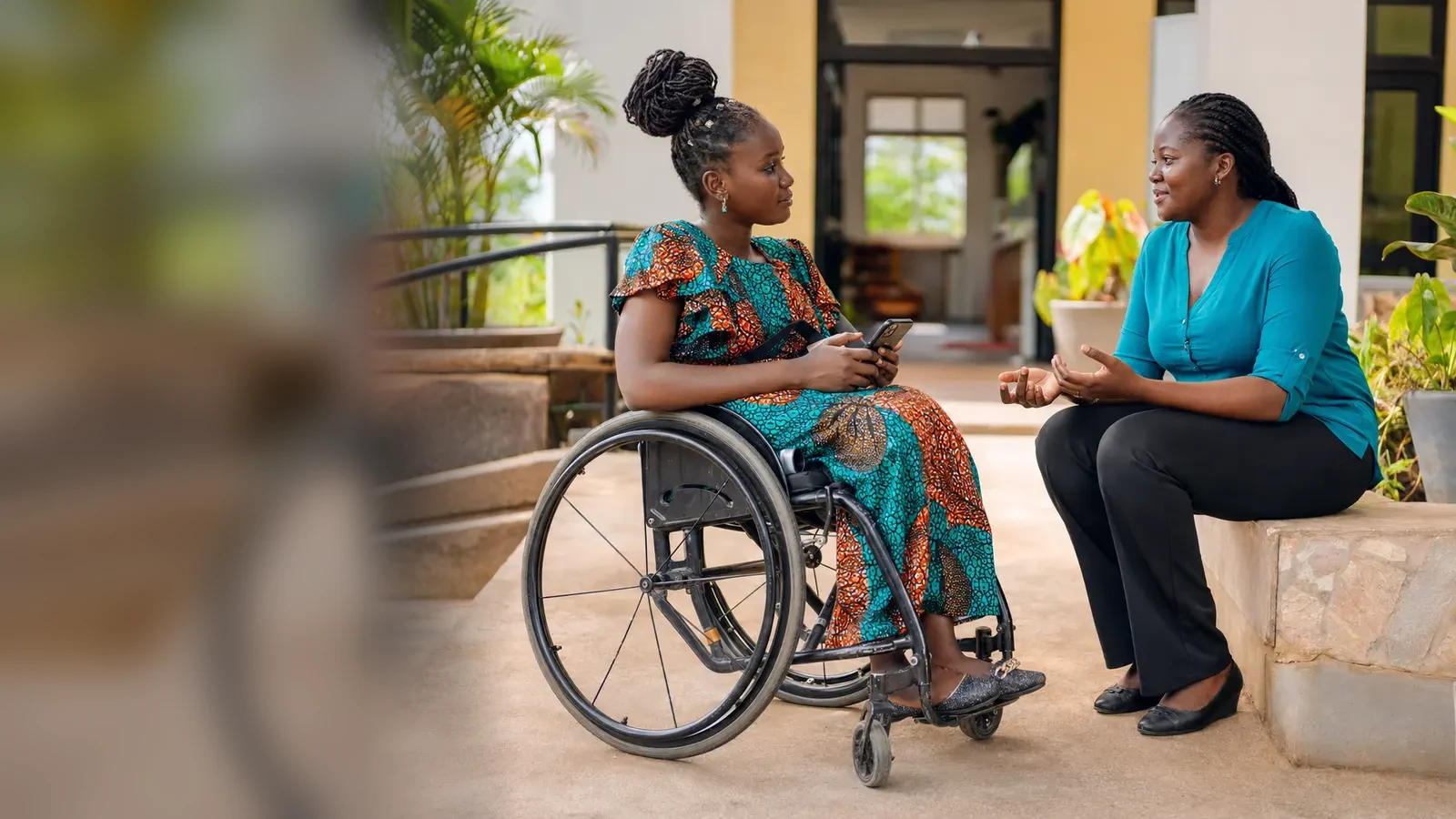 A Black Ugandan wheelchair user in conversation with a support professional