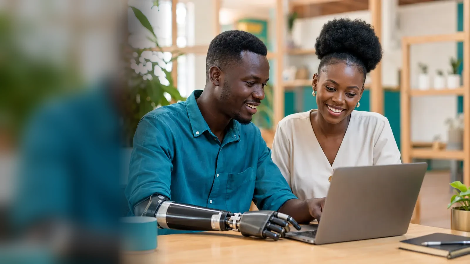 Two young Black Ugandan adults reviewing opportunities together on a laptop, with a prosthetic arm visible